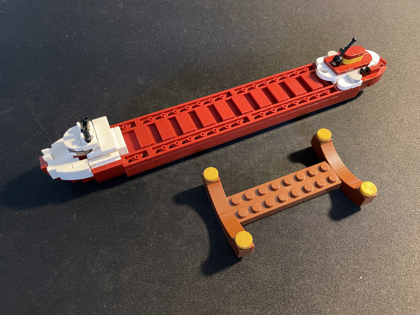 Red and white toy boat with a small brown dock on a dark surface.