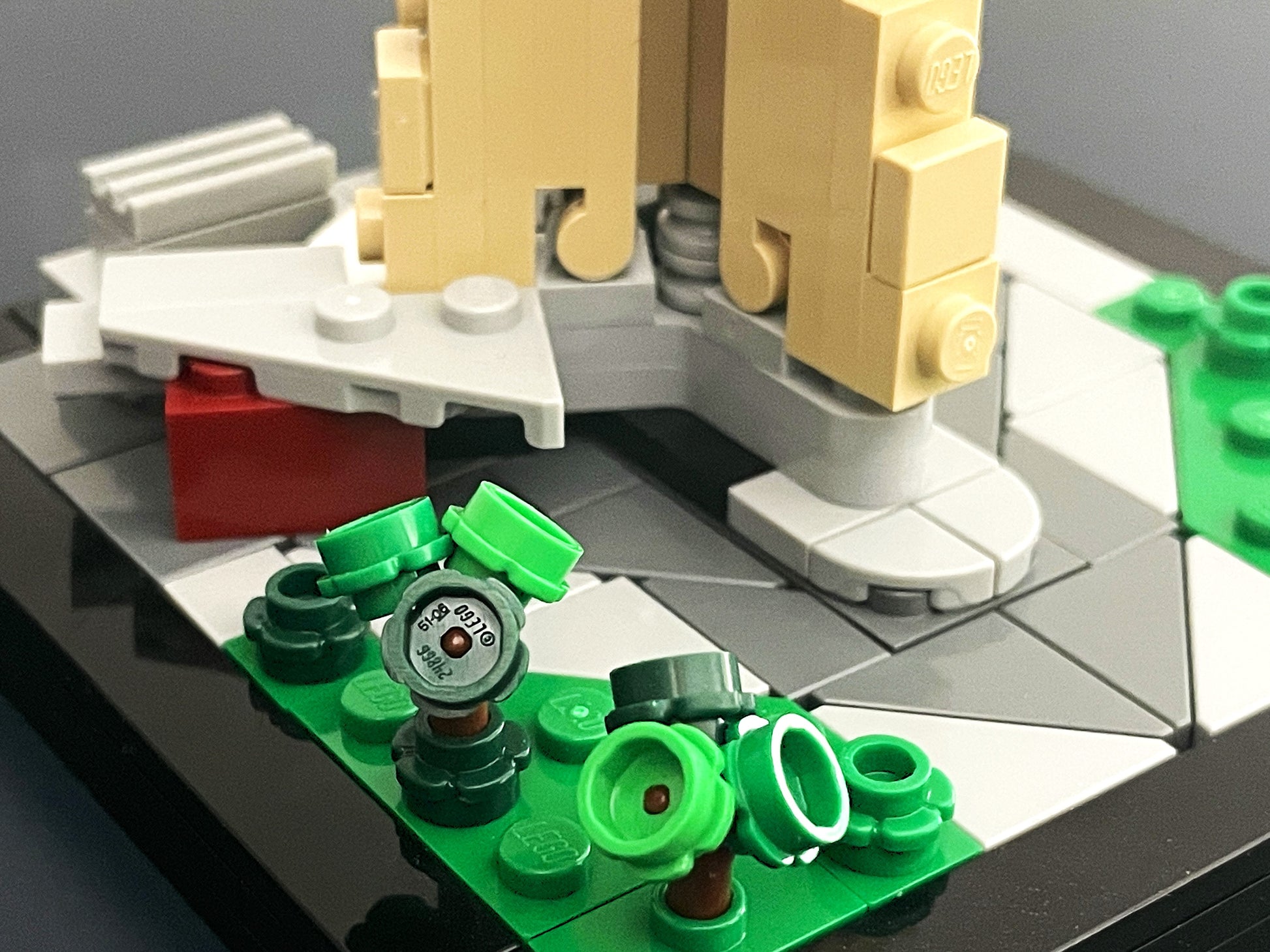 Close-up of a LEGO CN Tower model with green baseplate and various pieces on a reflective surface.